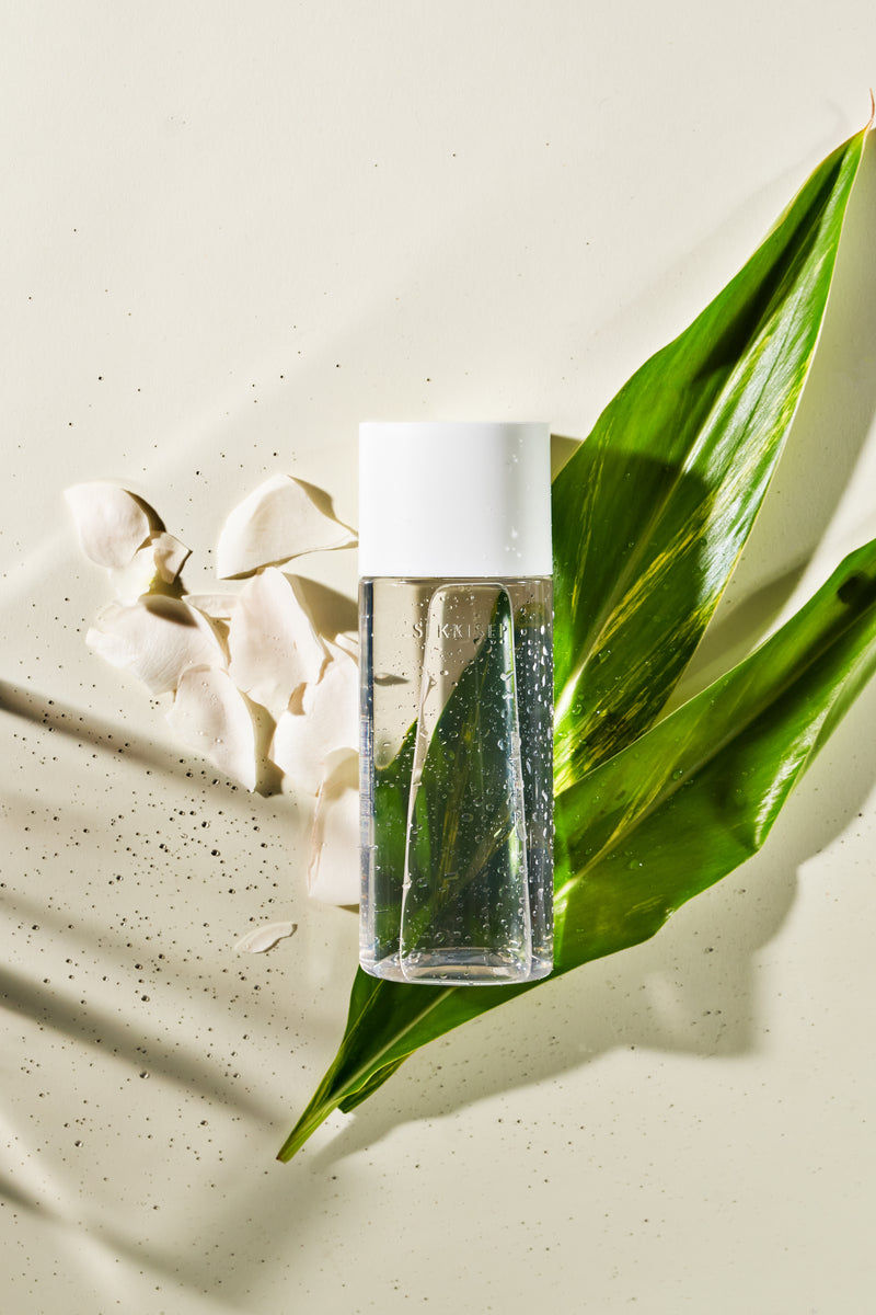 A product shot of Sekkisei Clear Wellness Balancing Liquid with white flower petals and green leaves in the background. 