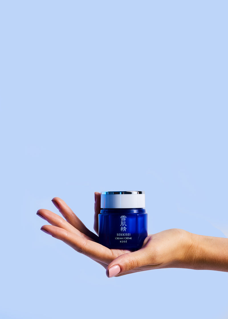 Showing a person's hand holding Sekkisei Cream against a light blue background. 